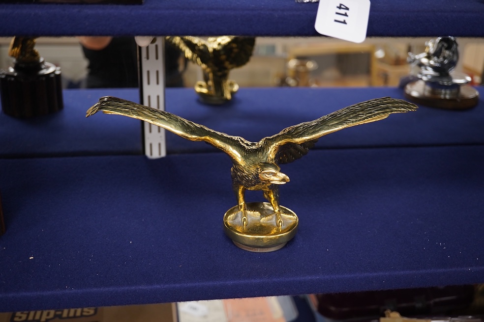 Two brass car mascots in the form of eagles, one mounted on a threaded radiator cap, the other mounted on a wooden base, the larger with a wingspan of 31cm. Condition - fair, one eagle with bent wing.